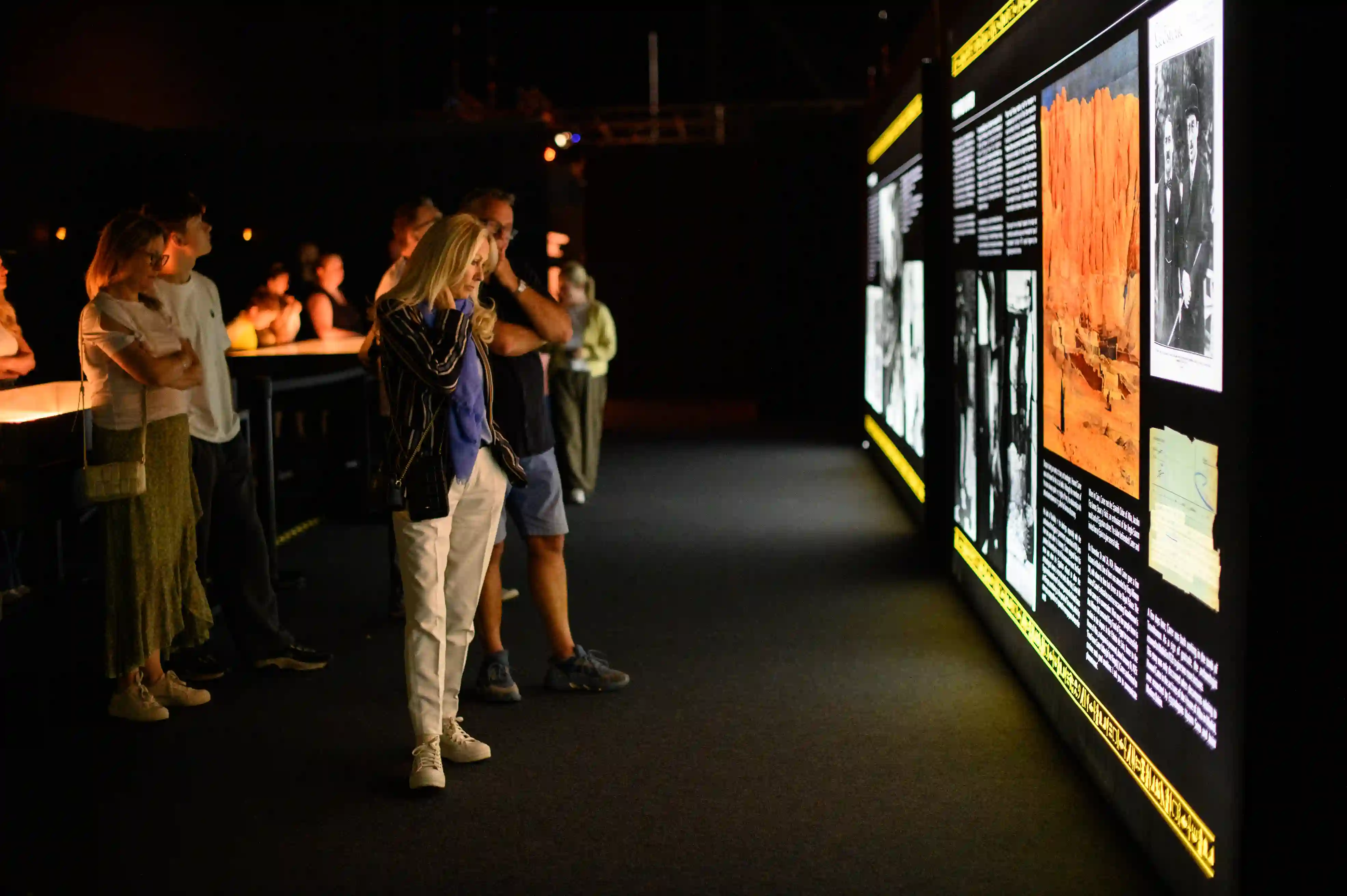 Tutankhamun-The-Immersive-Exhibition-Helsinki-6 Kävijät lukevat valaistuja infoseiniä, joilla on mustavalkoisia arkistokuvia ja tekstejä Tutankhamonin haudan löytymisestä.