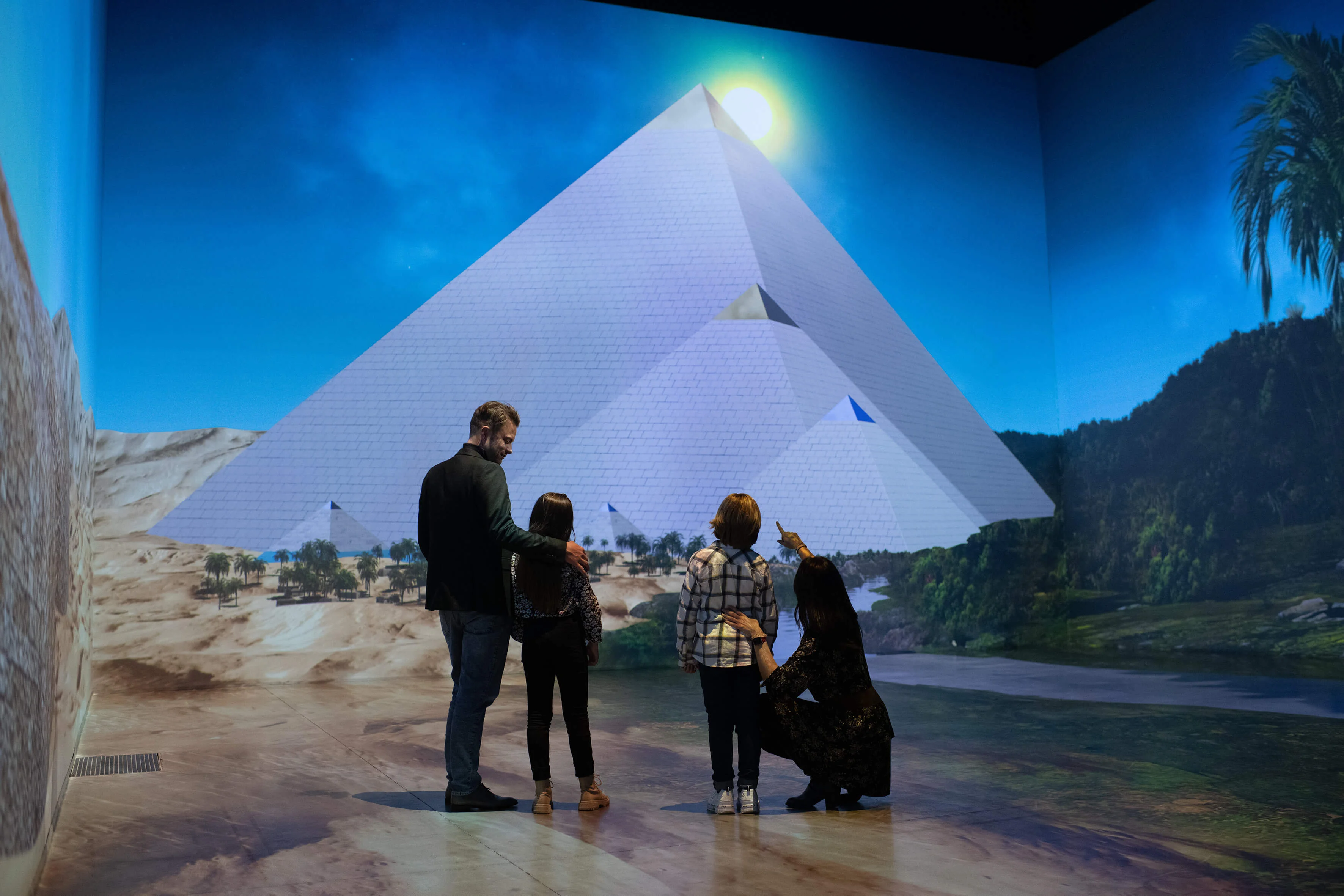 Perhe katselee yhdessä suurta pyramidi- ja Niili-projektiota vehreän maiseman edessä.
